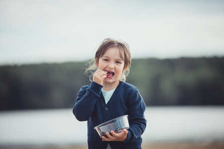 The girl eating blueberries from a glass bowl outdoorの写真素材