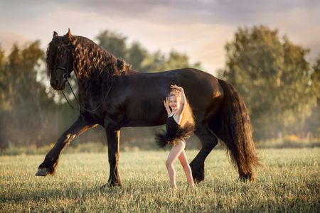Little ballerina girl with black friesian stallion at summer eveningの写真素材