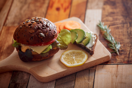 Dark burger with grain bread on dark ceramic plate, salad, rosemary and lemonの写真素材