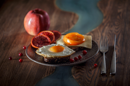 Grain bread with fried egg, tomato, cheese and bacon on ceramic plate with red orange to desertの写真素材