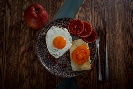 Grain bread with fried egg, tomato, cheese and bacon on ceramic plate with red orange to desertの写真素材
