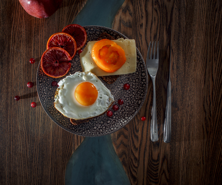 Grain bread with fried egg, tomato, cheese and bacon on ceramic plate with red orange to desertの写真素材