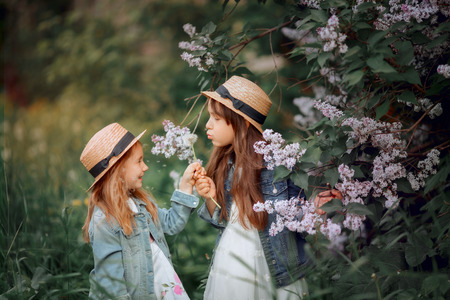 Little sisters outdoor portrait near lilac tree at spring eveningの写真素材