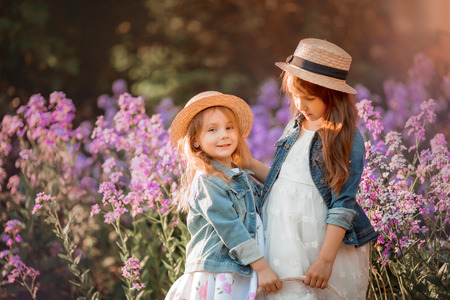 Little sisters outdoor portrait in a pink flowers at sunsetの写真素材
