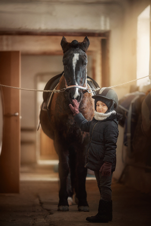 Teenage girl standing near black horse in a stableの写真素材