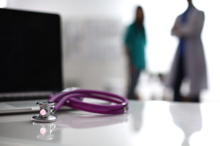 Laptop and stethoscope on the desk , doctors standing in the background.の写真素材