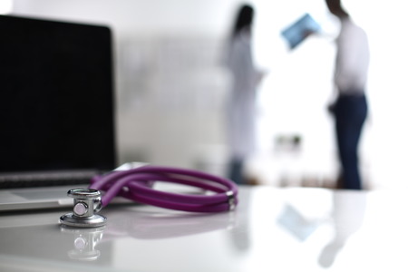 Laptop and stethoscope on the desk , doctors standing in the background.の写真素材