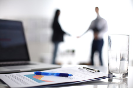 Laptop computer with folder on the desk ,two businesspeople standing in the background.の写真素材