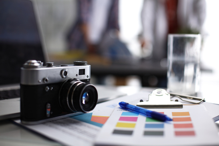 Laptop and camera on the desk , two businesspeople standing in the background.の写真素材