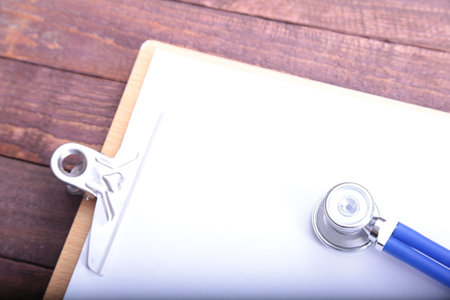 Closeup of a medical stethoscope with folder on wooden background.