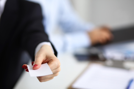 Female hand holding a blank business card sitting on the desk, selective focus.の写真素材