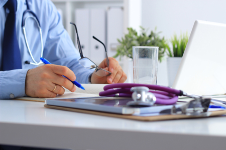 Male doctor with medical stethoscope using a laptop, sitting at his deskの写真素材