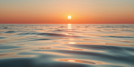 AI Generated. Orange light reflects on calm sea water as the sun sets over the horizonの素材