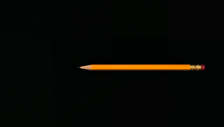 A single, yellow pencil lies horizontally against a deep black background, accented by faint, scattered light points. Minimalist and balanced composition.の素材