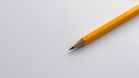 A simple yellow pencil lays diagonally on a textured white background. The light creates subtle shadows that enhance the texture. Clean composition, minimalist aesthetic.の素材