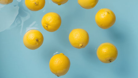 A refreshing composition featuring ripe, yellow spheres floating on a soft blue textured surface, creating a tranquil scene of simple beauty and freshness.の素材