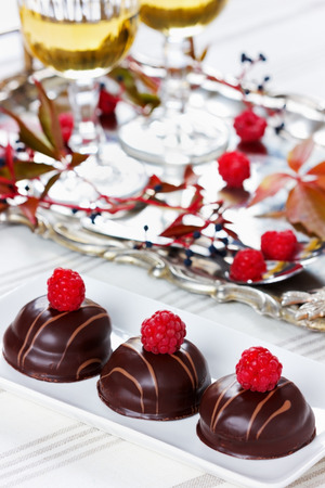 chocolate cake decorated with raspberries in white plate with glasses of white wine on vintage trayの写真素材