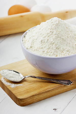 Flour in ceramic bowl with eggs and rolling pin on a white wooden backgroundの写真素材