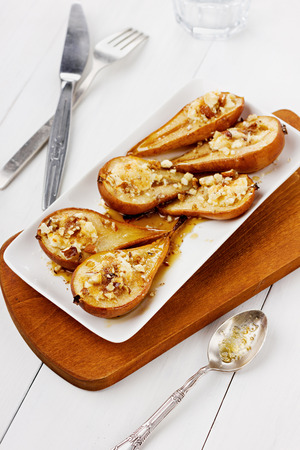 Dessert from the baked pears with honey and nuts in a white plate on a wooden backgroundの写真素材