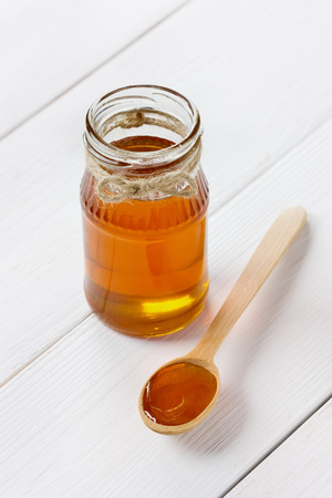 Honey in a wooden spoon and jar on a white backgroundの写真素材