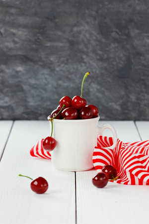 white mug of fresh cherries on wooden tableの写真素材