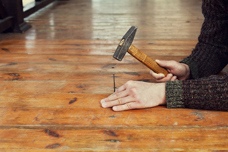 man hands drive nail with a hammer in wooden floor, carpentry, toned imageの写真素材