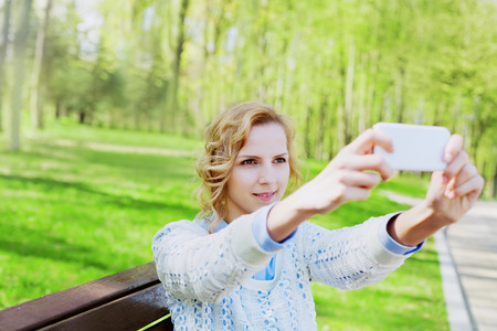 young girl student having fun and taking selfie photo on smartphone camera outdoor in green park in sunny day, teenage trand, people conceptの写真素材