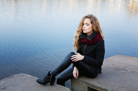 beautiful blonde woman with long curly hair sitting on the banks of the blue river water having closed eyes and enjoying silence, meditation or relaxation conceptの写真素材