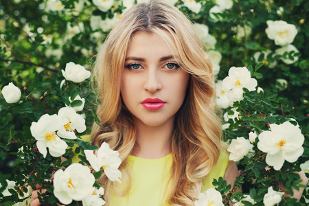 beautiful happy woman with long curly hair smells white roses flower outdoors, closeup portrait of sensual blonde girl face, elegant lady in blossom garden, vintage toningの写真素材
