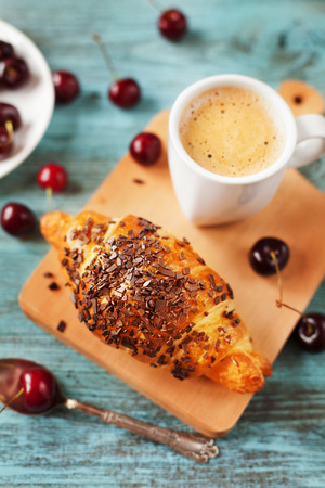 Tasty breakfast with fresh croissant, coffee and cherries on a wooden table, selective focus on croissantの写真素材