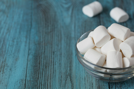 White soft marshmallows in glass bowl on blue wooden background, selective focusの写真素材