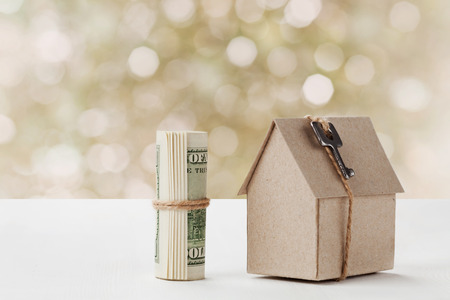 Model of cardboard house with key and dollar bills. House building, loan, real estate, cost of housing or buying a new home concept.の写真素材