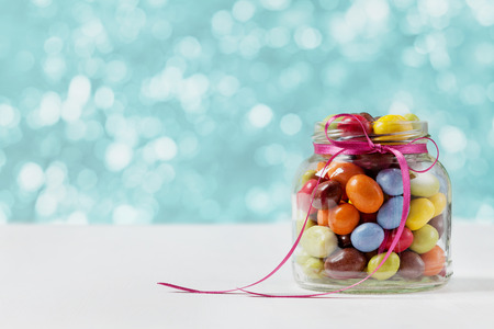 Colorful candy jar decorated with a bow against blue bokeh background, birthday conceptの写真素材