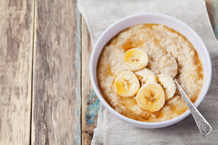 Bowl of oatmeal porridge with banana and caramel sauce on rustic table, hot and healthy breakfast every day, diet foodの写真素材