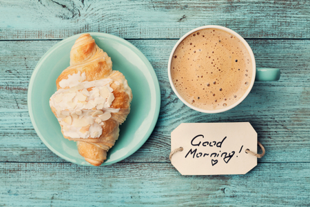 Coffee mug with croissant and notes good morning on turquoise rustic table from above, cozy and tasty breakfast, vintage tonedの写真素材