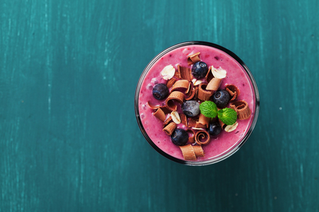 Healthy breakfast of smoothie, dessert, yogurt or milkshake with frozen blueberry and oats decorated grated chocolate and mint leaves on wooden rustic table, top viewの写真素材