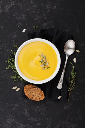 Pumpkin soup decorated seeds and thyme in white bowl on black table top view. Flat lay styling.の写真素材