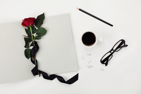 Womens working space with cup of coffee, pencil, empty notebook, glasses, black ribbon and rose flower on white table top view. Flat lay styling.の写真素材