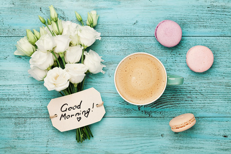 Coffee mug with macaron, white flowers and notes good morning on blue rustic table from above. Beautiful breakfast. Flat lay.の写真素材