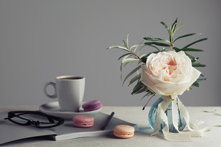 Morning still life with vintage rose in a vase, coffee and macarons on a light table. Beautiful and cozy breakfast.の写真素材