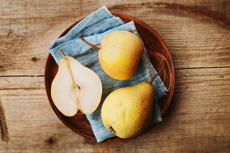 Ripe organic pears in earthenware dish on rustic wooden table top viewの写真素材