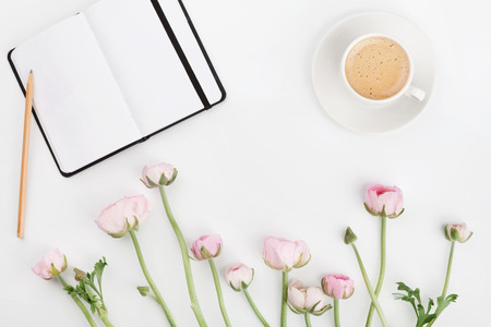 Beautiful spring Ranunculus flowers, empty notebook and cup of coffee on white desk from above. Greeting card. Breakfast. Pastel color. Clean space for text. Flat lay style.の写真素材