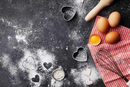 Baking background with flour, rolling pin, eggs, and heart shape on dark kitchen table top view for Valentines day cooking. Flat lay style.の写真素材