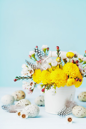 Easter greeting card with colorful flowers, feather and quail eggs on blue background. Beautiful spring composition.の写真素材