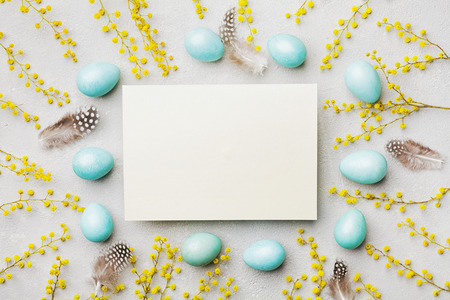 Painted Easter eggs, mimosa flower and paper card on vintage stone background top view in flat lay style. Empty space for text.の写真素材