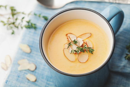 Dietary vegetable cream soup from carrot and potato decorated almonds flakes in blue bowl on rustic...