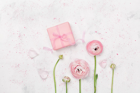 Gift or present box and beautiful ranunculus flower on white table from above for wedding mockup or greeting card on mothers day in flat lay style.の写真素材