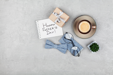 Happy Fathers Day background with morning coffee cup, gift, glasses and bowtie on stone gray desk top view in flat lay style.の写真素材
