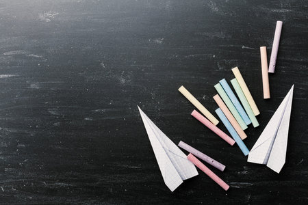 Back to school concept. Colorful chalks and paper airplane on blackboard from above.の写真素材