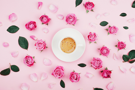 Creative card with coffee cup, green leaves and beautiful pink rose flowers on pastel background from above in flat lay style. Fashion and cozy breakfast.の写真素材